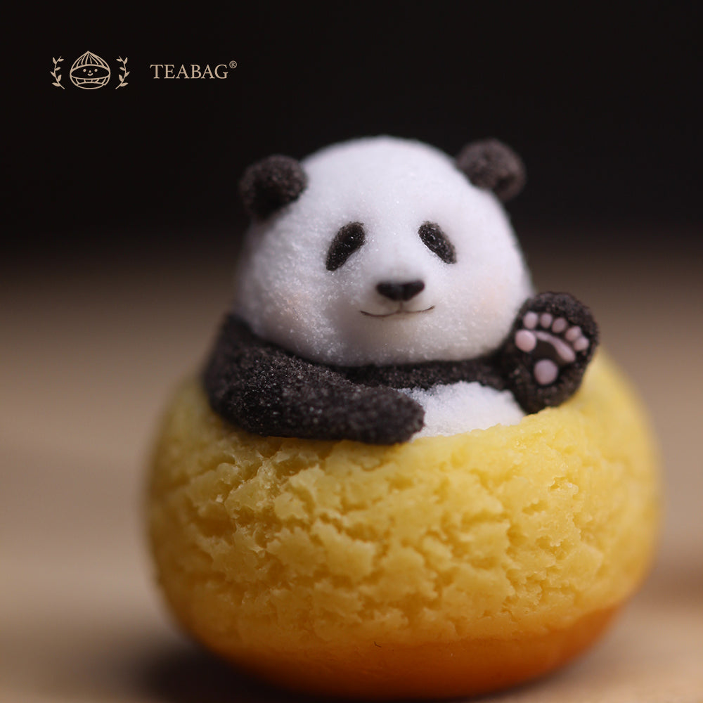 Complete front view of the waving Panda Cream Puff miniature without jewelry fittings, showing the raised paw, full golden cream puff and TEABAG logo in a square photograph.