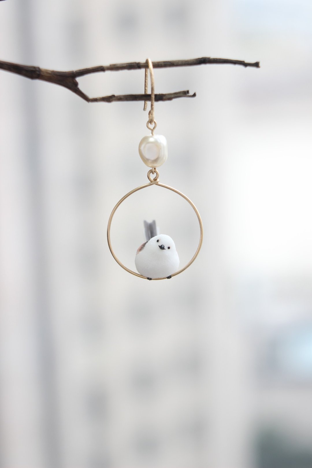 A tiny white long-tailed tit perched inside a gold-tone hoop earring